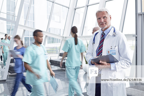 Portrait confident male doctor with clipboard in busy hospital lobby