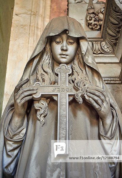 Pictures of a borgeoise realistic style stone sculpture of a girl holding a crucifix on the Poggi Family Tomb. The monumental tombs of the Staglieno Monumental Cemetery,  Genoa,  Italy.
