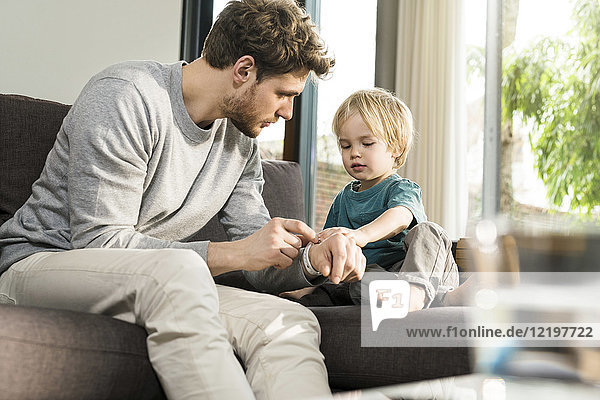 Son examining father's smartwatch on couch at home