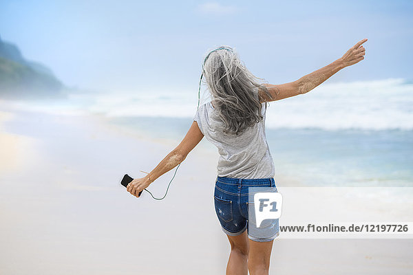 Senior woman with headphones dancing on the beach
