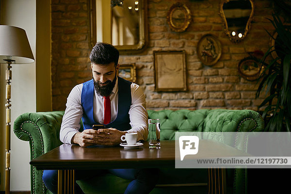 Fashionable young man sitting on couch in a cafe using cell phone