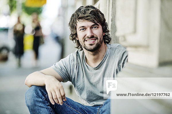 Porträt eines lächelnden jungen Mannes  der im Freien sitzt.