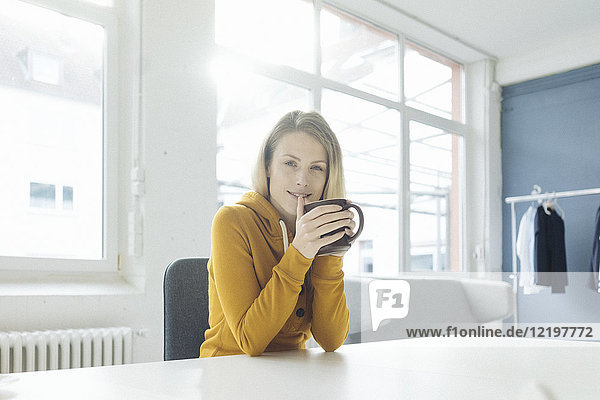 Porträt der Modedesignerin am Schreibtisch in ihrem Atelier bei einer Tasse Kaffee