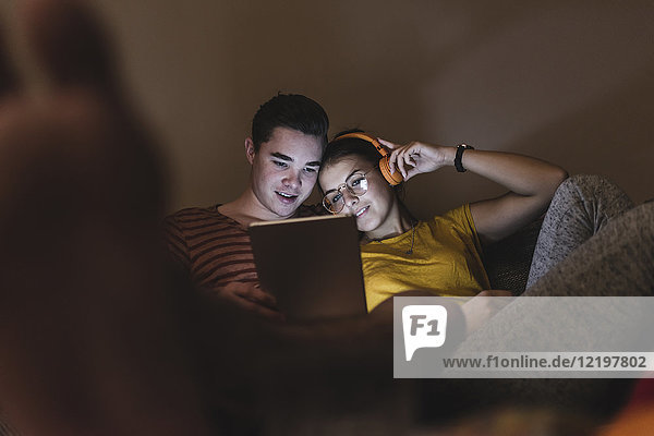 Couple with headphones and tablet relaxing on couch at home