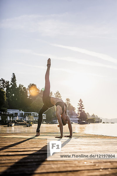 Frau praktiziert Yoga am Steg eines Sees