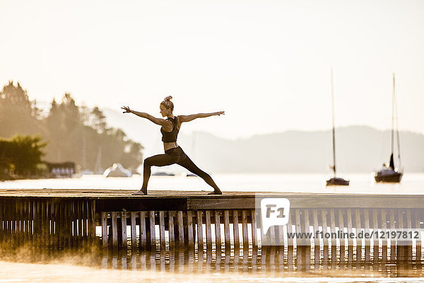 Woman practicing yoga on jetty at a lake