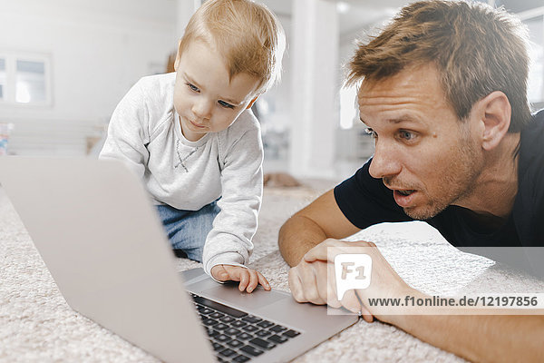 Erstaunlicher Vater mit kleiner Tochter  die den Laptop auf dem Boden benutzt.