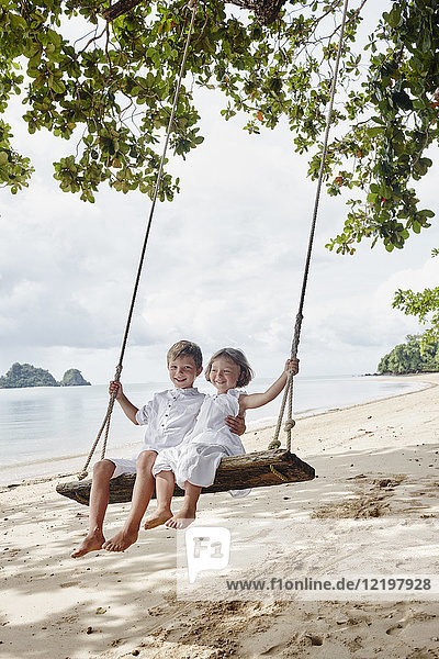 Thailand  Ko Yao Noi  glücklicher Junge und kleines Mädchen auf einer Schaukel am Strand