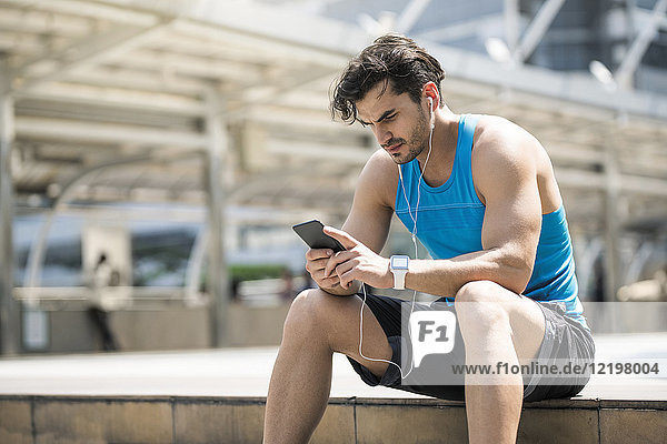 Runner wearing earphones  checking messages on his smartphone