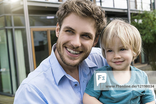 Portrait of smiling father with son in front of their home