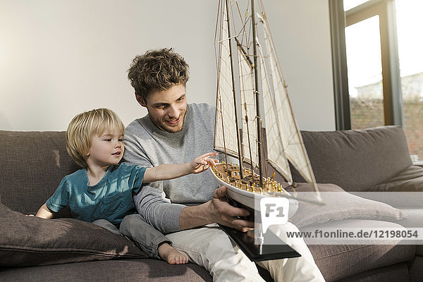 Father and son looking at toy model ship on couch at home