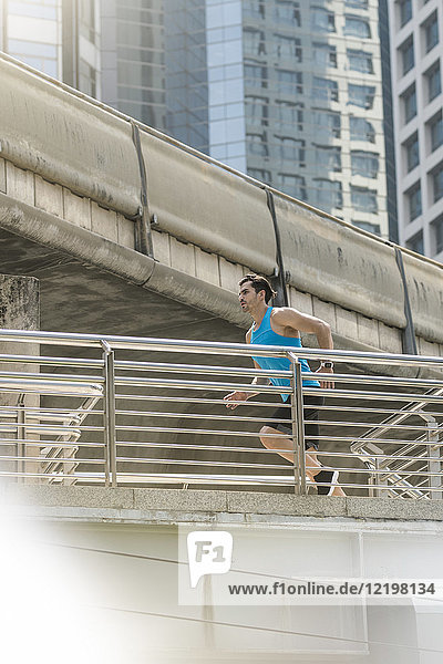 Läufer in blauem Fitness-Shirt über moderne Brücke laufend