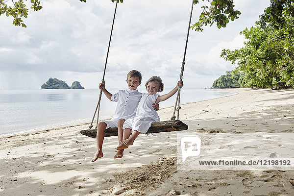 Thailand  Ko Yao Noi  glücklicher Junge und kleines Mädchen auf einer Schaukel am Strand