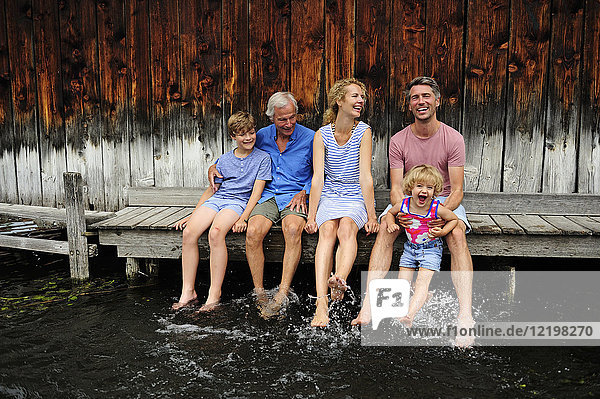 Familie sitzt zusammen auf einem Steg und spritzt mit Wasser.