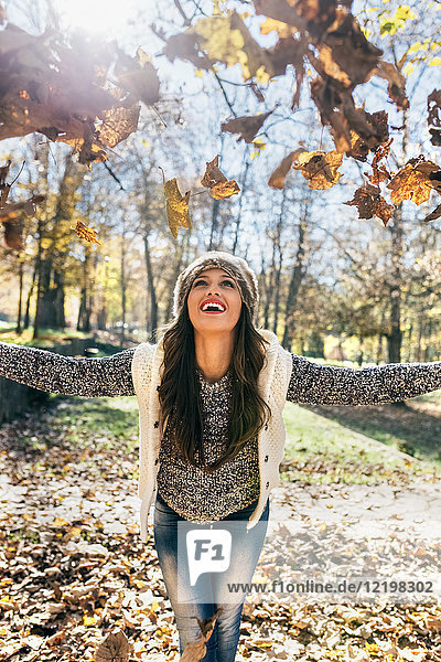 Beautiful happy woman having fun with leaves in an autumnal forest