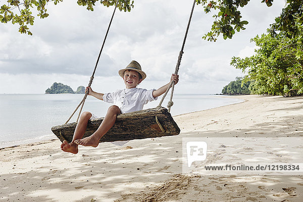 Thailand  Ko Yao Noi  glücklicher Junge auf einer Schaukel am Strand