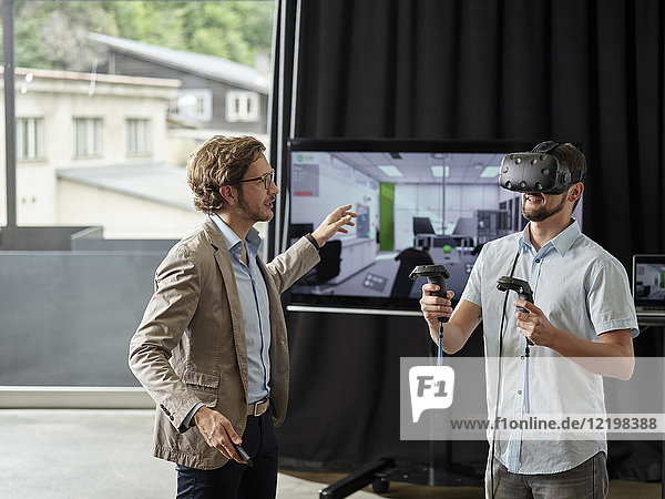 Mann im Gespräch mit Kollegen mit VR-Brille vor dem Bildschirm