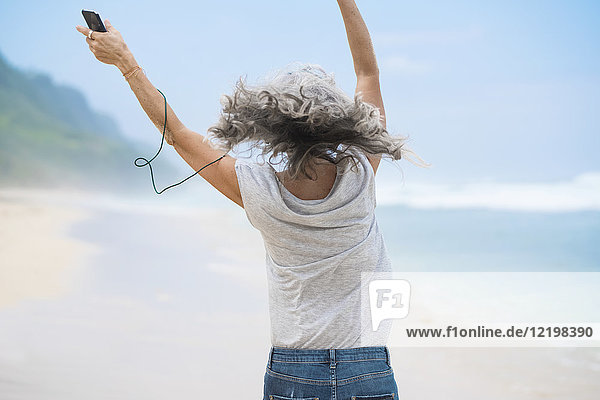Seniorin mit Kopfhörer tanzt am Strand