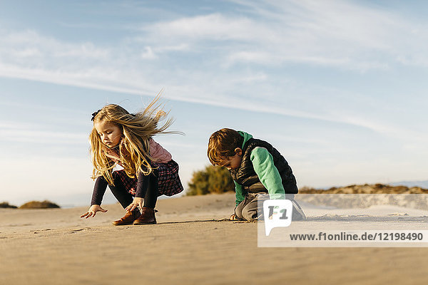 Two children playing with the sand on the beach in winter