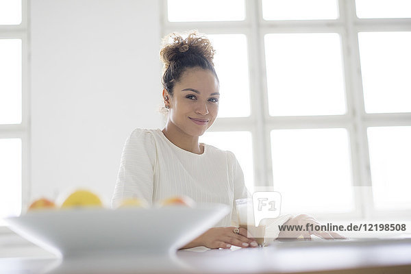 Porträt einer lächelnden jungen Frau  die mit einem Glas Kaffee am Tisch sitzt.