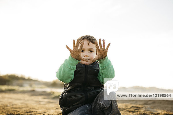 Junge  der im Winter am Strand spielt und seine schmutzigen Hände zeigt.