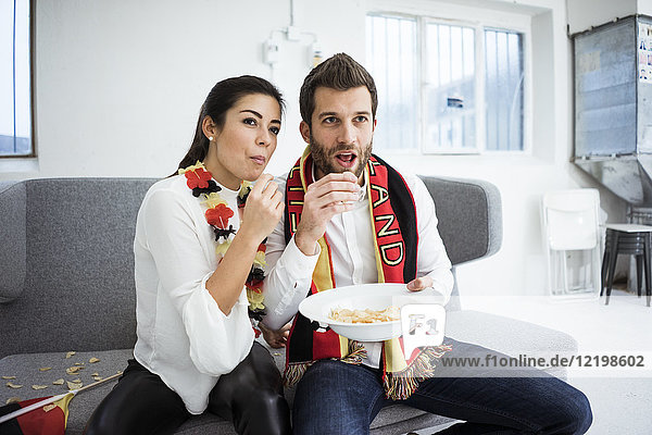 Deutsches Fußballfanpaar sitzt auf der Couch isst Chips und schaut TV