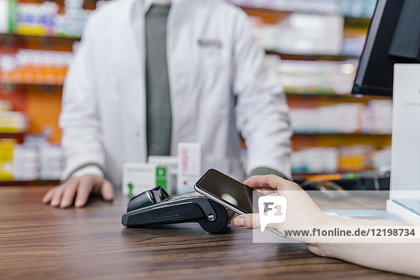 Close-up of customer paying cashless with smartphone in a pharmacy