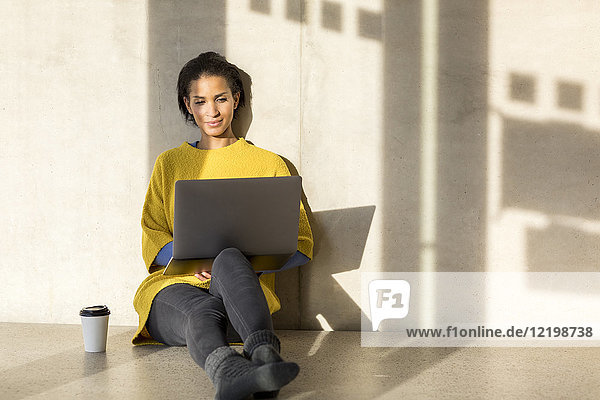 Porträt einer lächelnden jungen Frau auf dem Boden sitzend mit Laptop