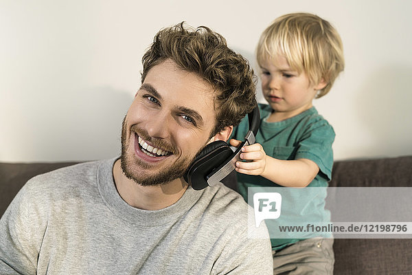 Glücklicher Vater und Sohn mit Kopfhörer auf der Couch zu Hause