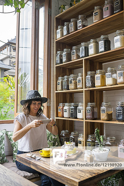 Frau mit Hut im Café beim Fotografieren von Lebensmitteln mit Smartphone