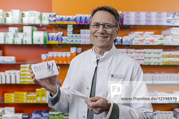 Porträt eines lächelnden Apothekers mit Tablettenpackung und Rezept in der Apotheke