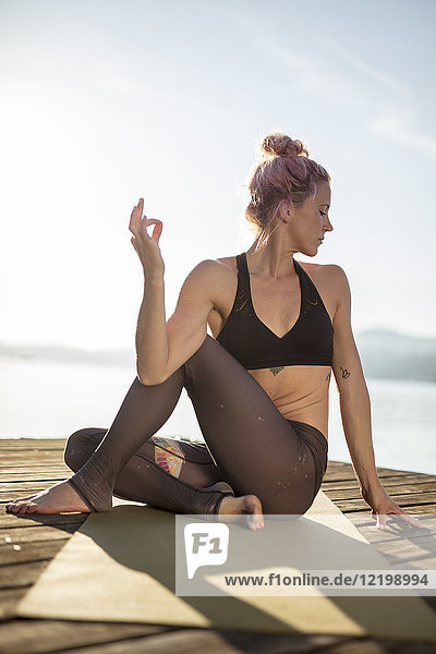 Frau sitzt auf einem Steg am See und übt Yoga.