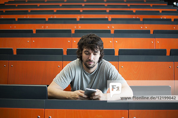 Portrait eines Studenten im Hörsaal der Universität mit Blick auf das Handy