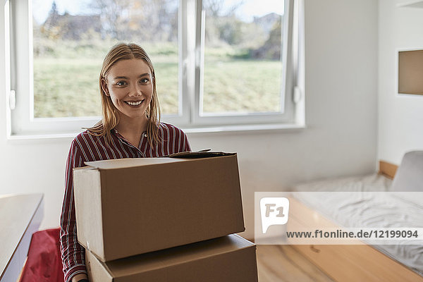 Portrait of smiling young woman carrying cardboard boxes