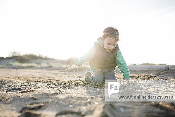 Junge spielt mit dem Sand am Strand im Winter