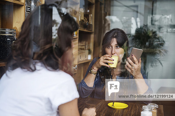 Frau mit Freundin in einem Café mit Smartphone und Kaffeetrinken