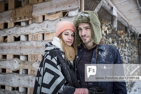 Portrait of couple in front of wood pile outdoors in winter