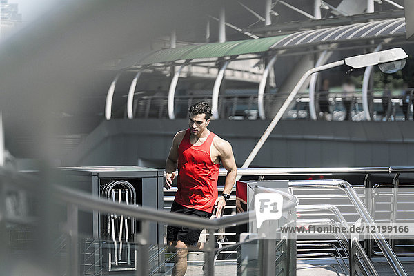 Läufer in rotem Fitness-Shirt über moderne Brücke laufend
