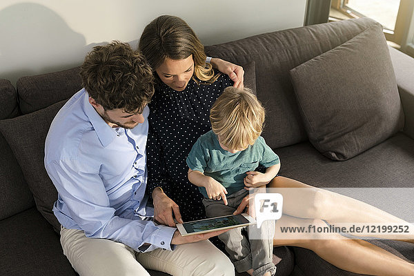 Parents and son sitting on sofa holding tablet at home