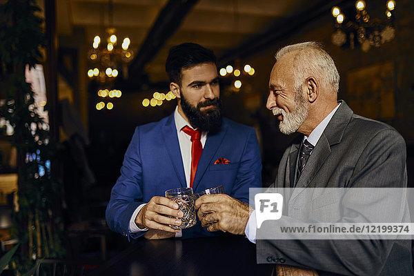 Two elegant men in a bar clinking tumblers
