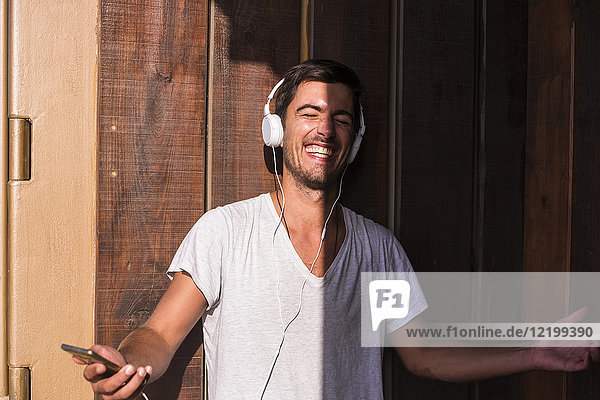 Happy young man with cell phone and headphones at wooden wall