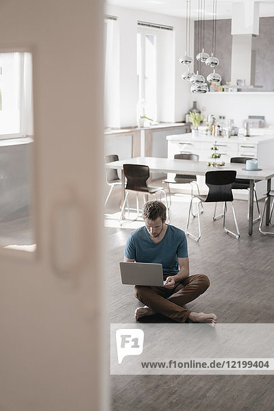 Man sitting on the floor in the kitchen working on laptop