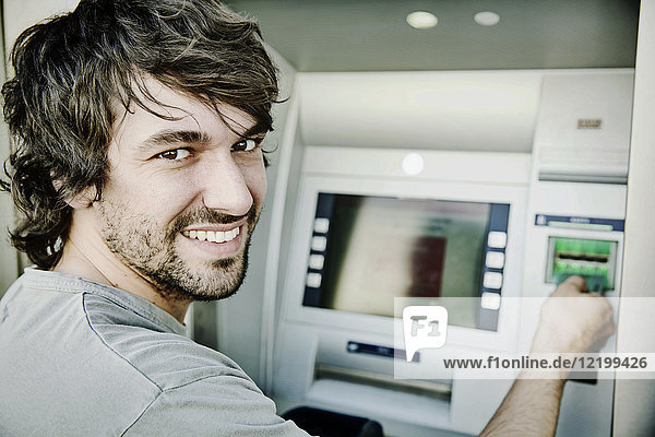 Porträt des lachenden jungen Mannes am Geldautomaten