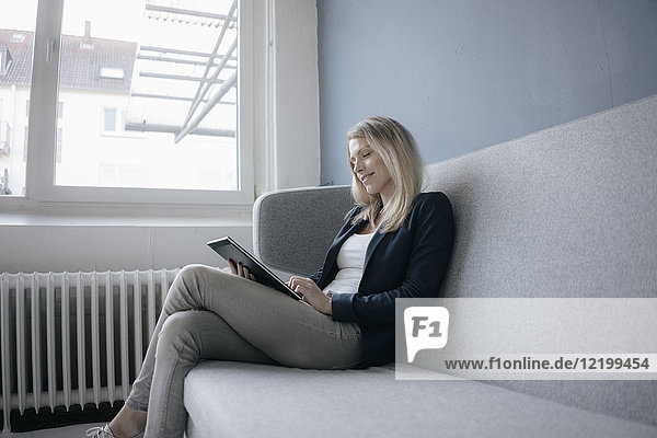 Smling Geschäftsfrau auf der Couch sitzend mit Tablette