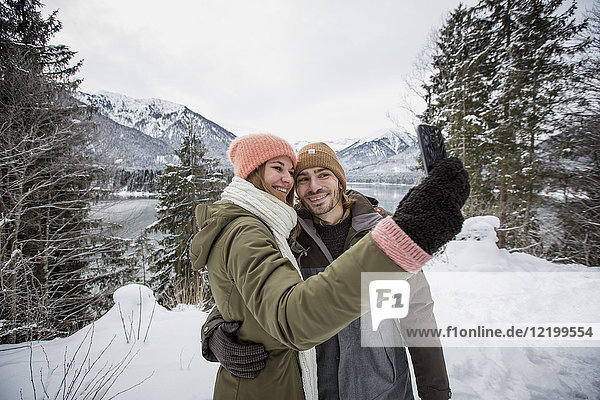 Smiling couple taking a selfie in alpine winter landscape with lake