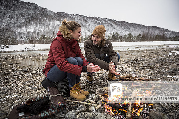 Couple on a trip in winter warming hands at camp fire