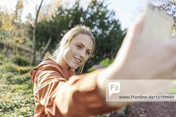 Porträt einer jungen Frau  die sich selbst mit dem Handy im Herbstpark fotografiert.