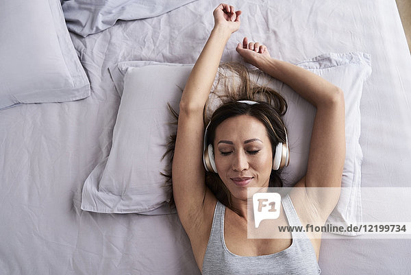 Entspannte Frau beim Musikhören im Bett