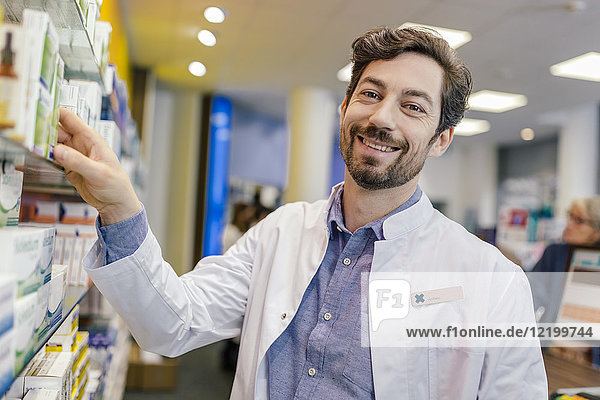 Portrait of smiling pharmacist with medicine at shelf in pharmacy