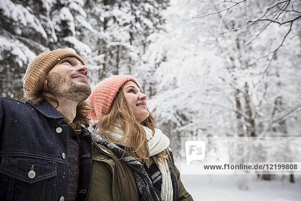 Lächelndes Paar im Winterwald  das den Schneefall beobachtet